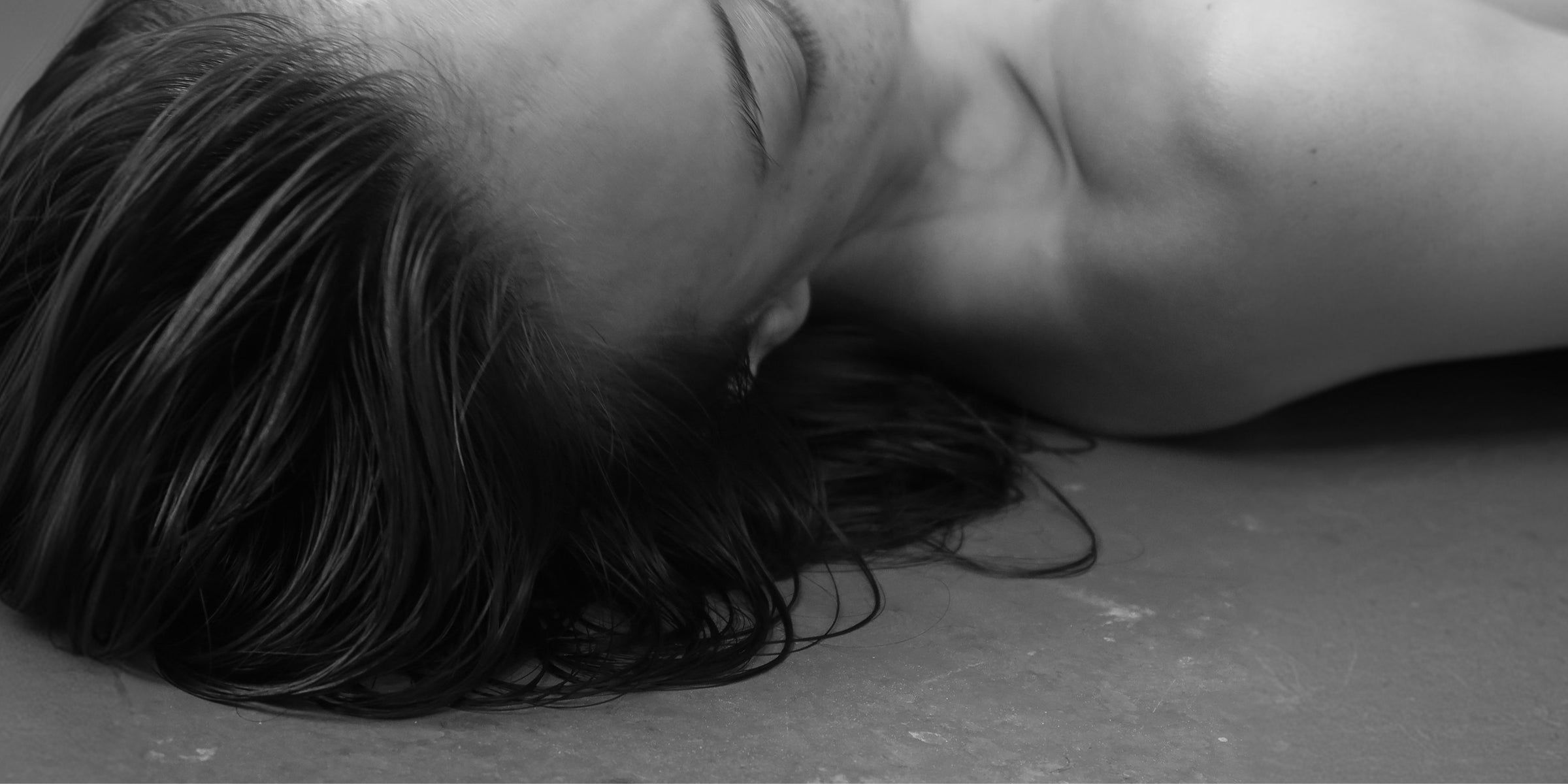 Black and white close-up of a person lying on a flat surface with hair covering part of their face.